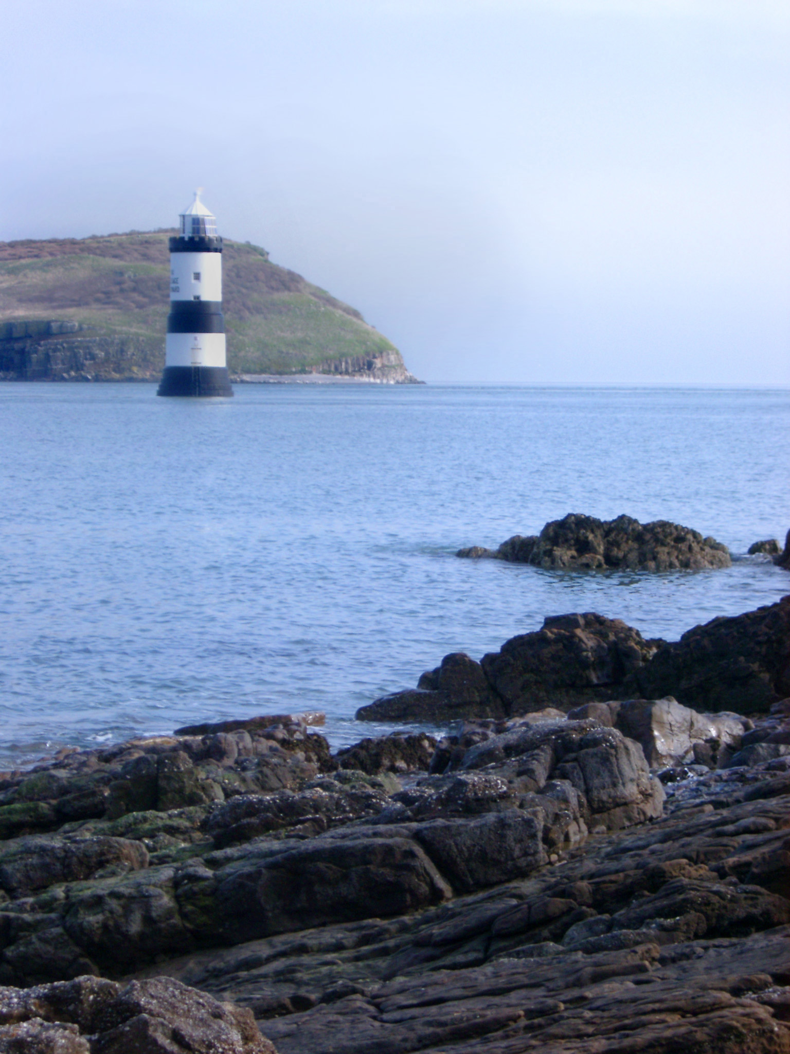 an image of View across the ocean of the distinctive black and white tower of the Trwyn Du Lighthouse, Anglesey, Wales