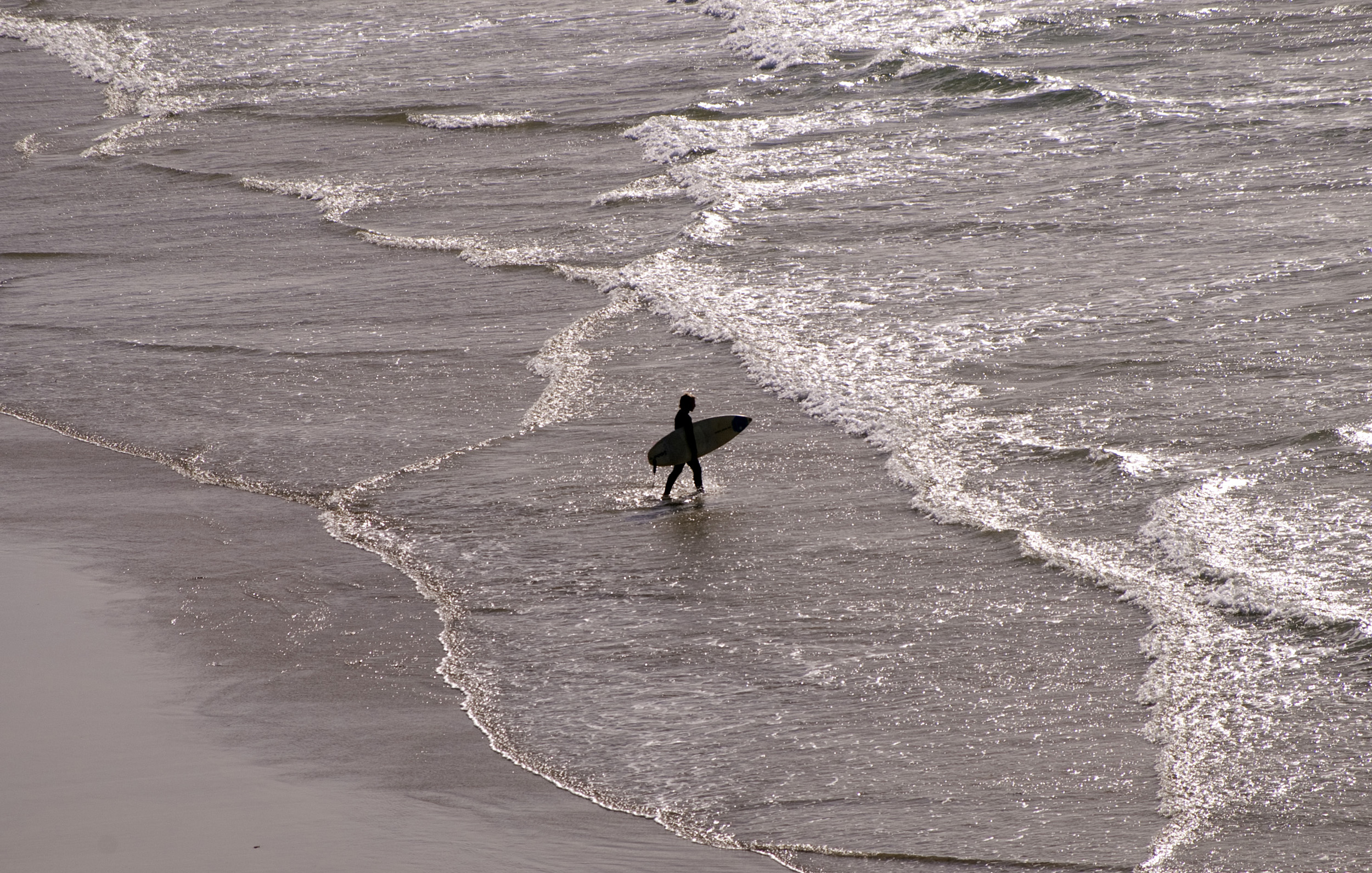 an image of silhouette of a surfer waking into the water with a surfboard
