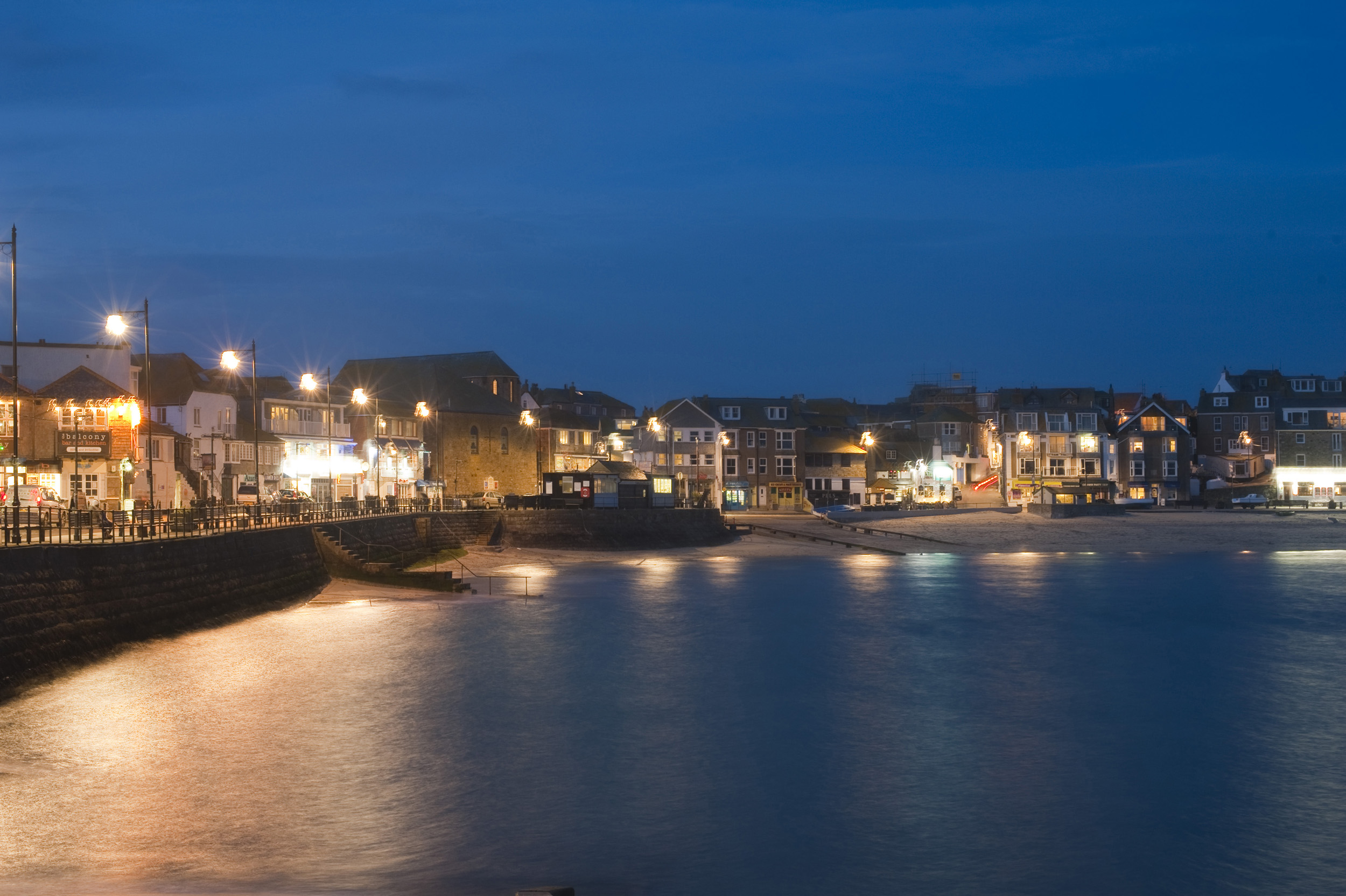an image of shops and bars brightly lit on the waterfront of saint ives, cornwall