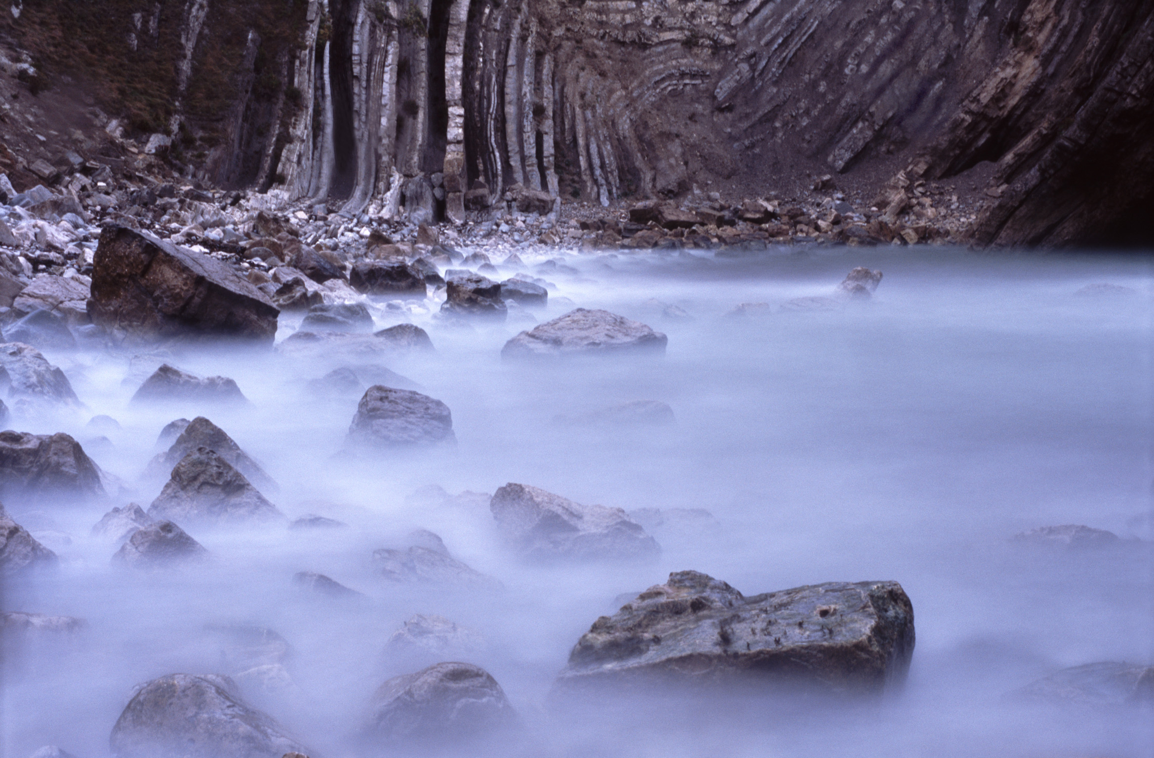 an image of long exposure image of water lapping rocks in stair hole, dorset.
