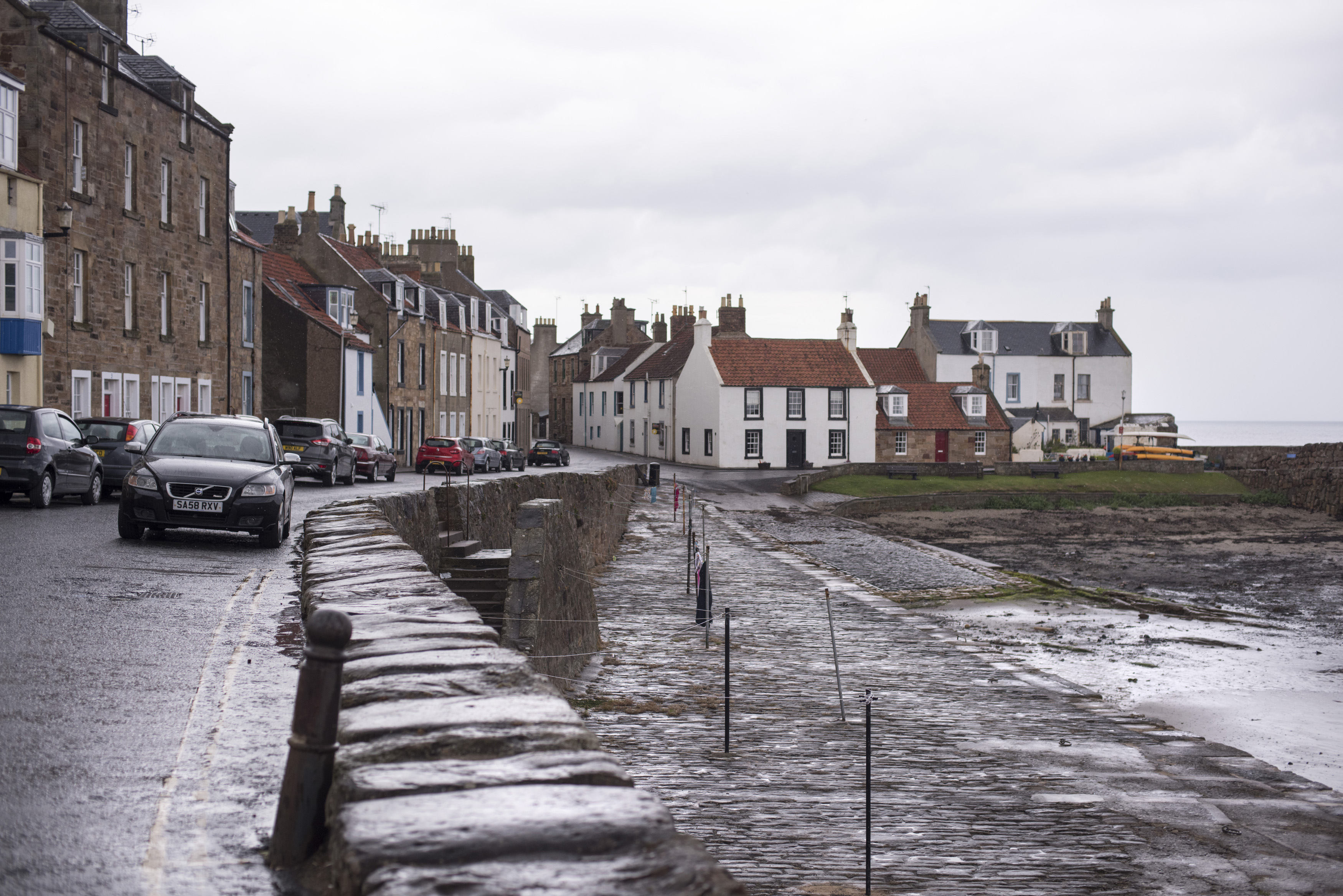 an image of Puddles of water on street, near apartments and automobiles under cloudy skies in Cellardyke, Scotland
