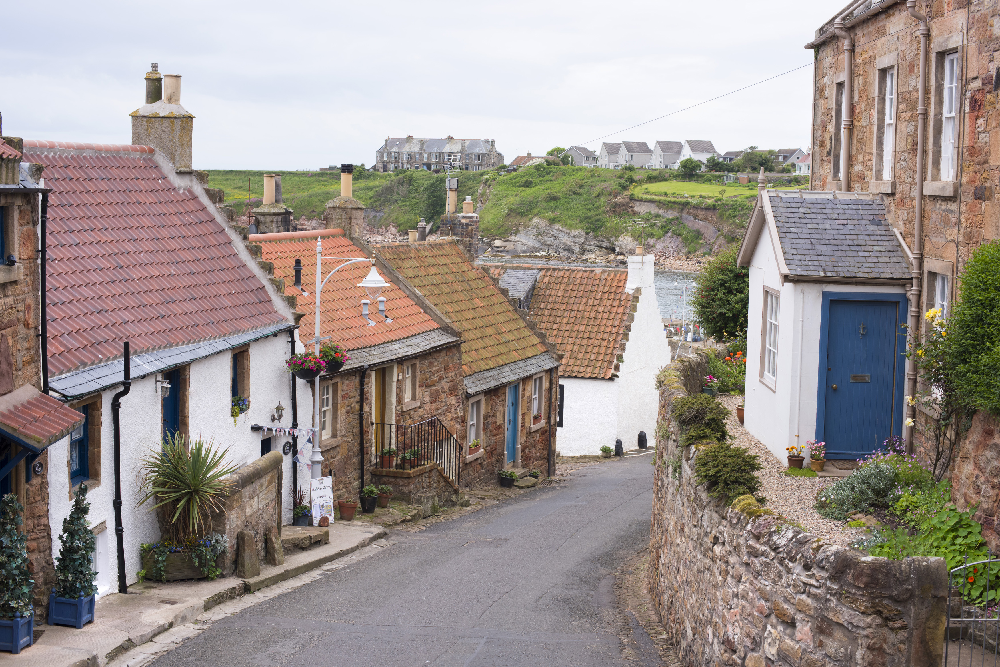 an image of Little traditional houses built close together on downward empty road in Crail, Scotland