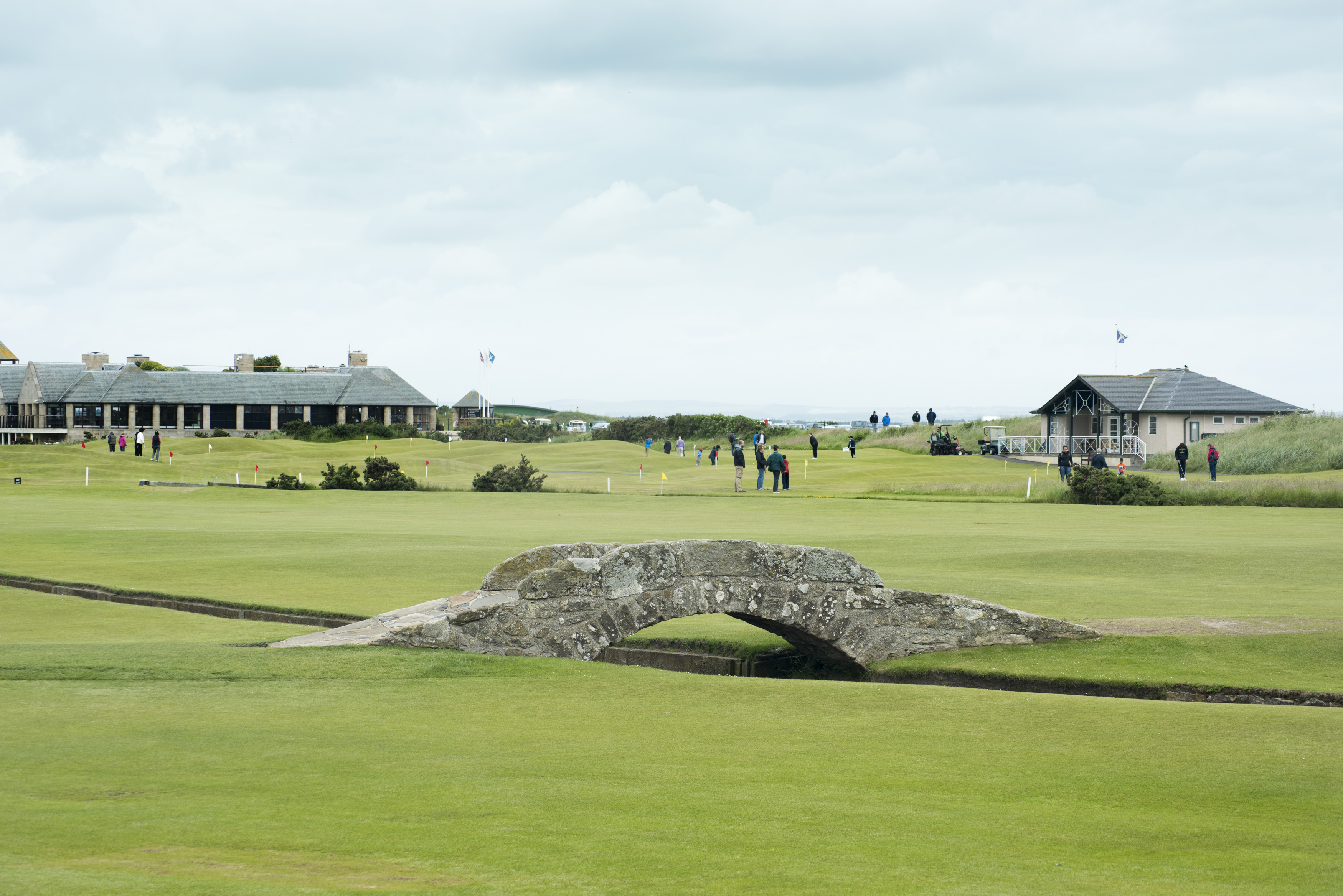 an image of Scenic view of beautiful scottish golf course with a short stone bridge and adjoining buildings in the distance