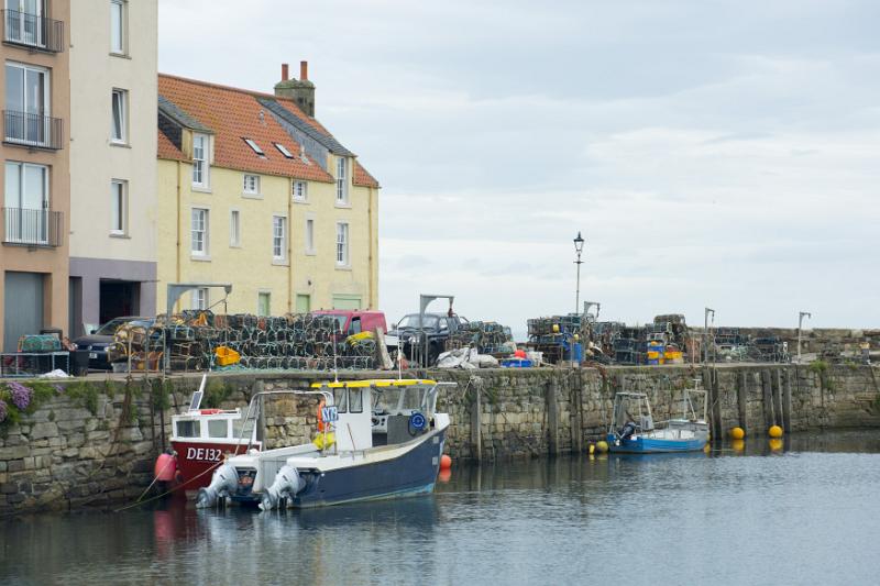 Fishing boats moored in the harbour, St Andrews, Scotland with stacked wire traps on the quay overlooked by waterfront apartments