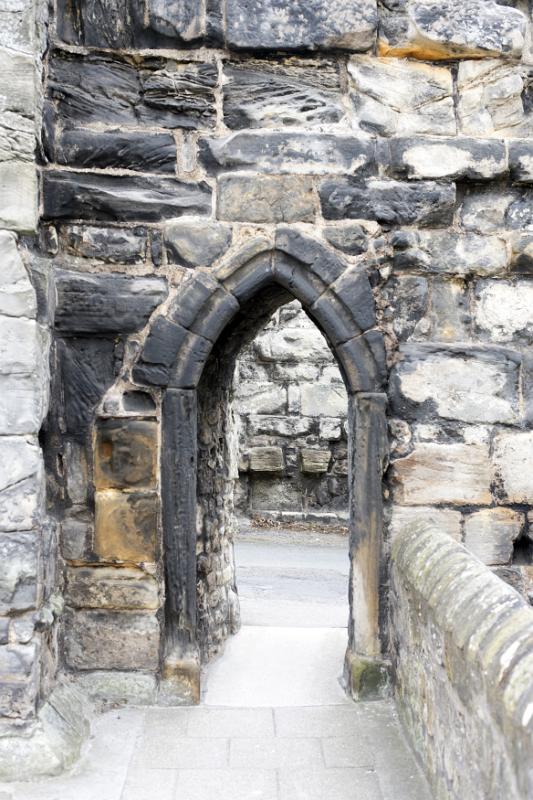 Medieval stone arch in an ancient building with a paved walkway leading through to a road behind