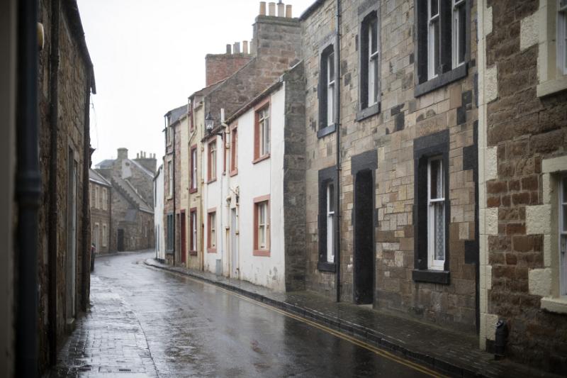Empty brick road on rainy day in old village lined with stone apartment houses in Scotland