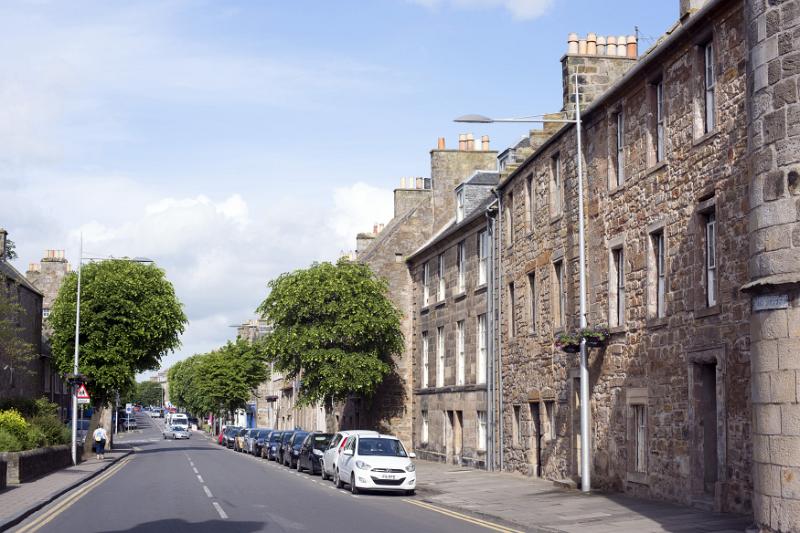 First person one point perspective view down paved road with old stone wall buildings in Saint Andrews, Scotland