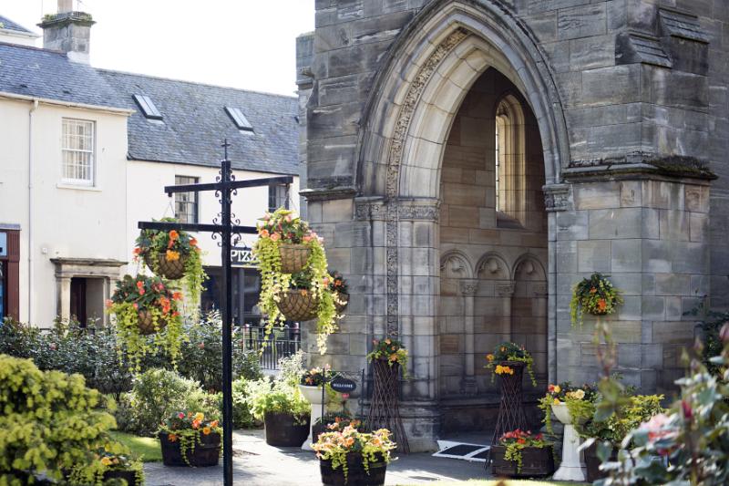 Flowing baskets near old stone church block entrance with arch in Saint Andrews, Scotland
