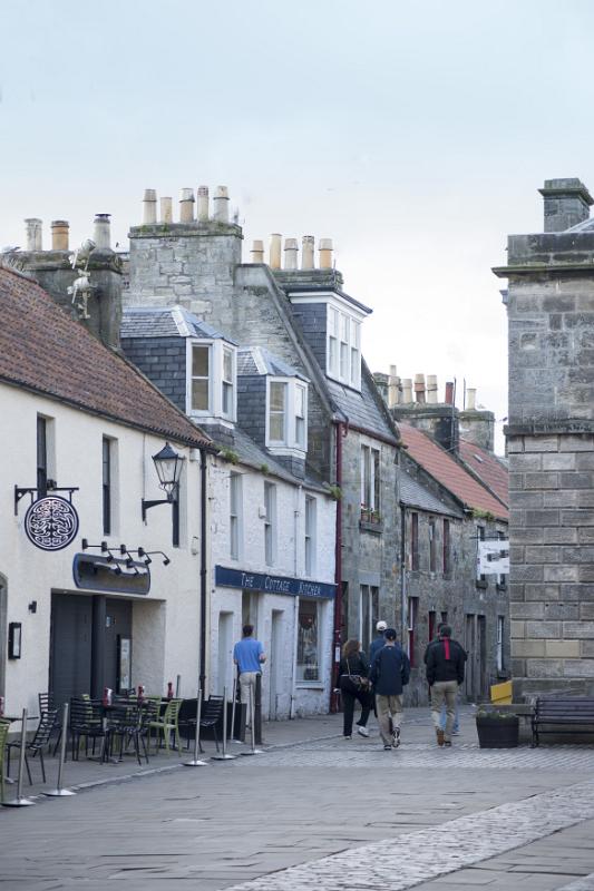 Rear view of various tourists walking down street in front of small cafe at Saint Andrews, Scotland