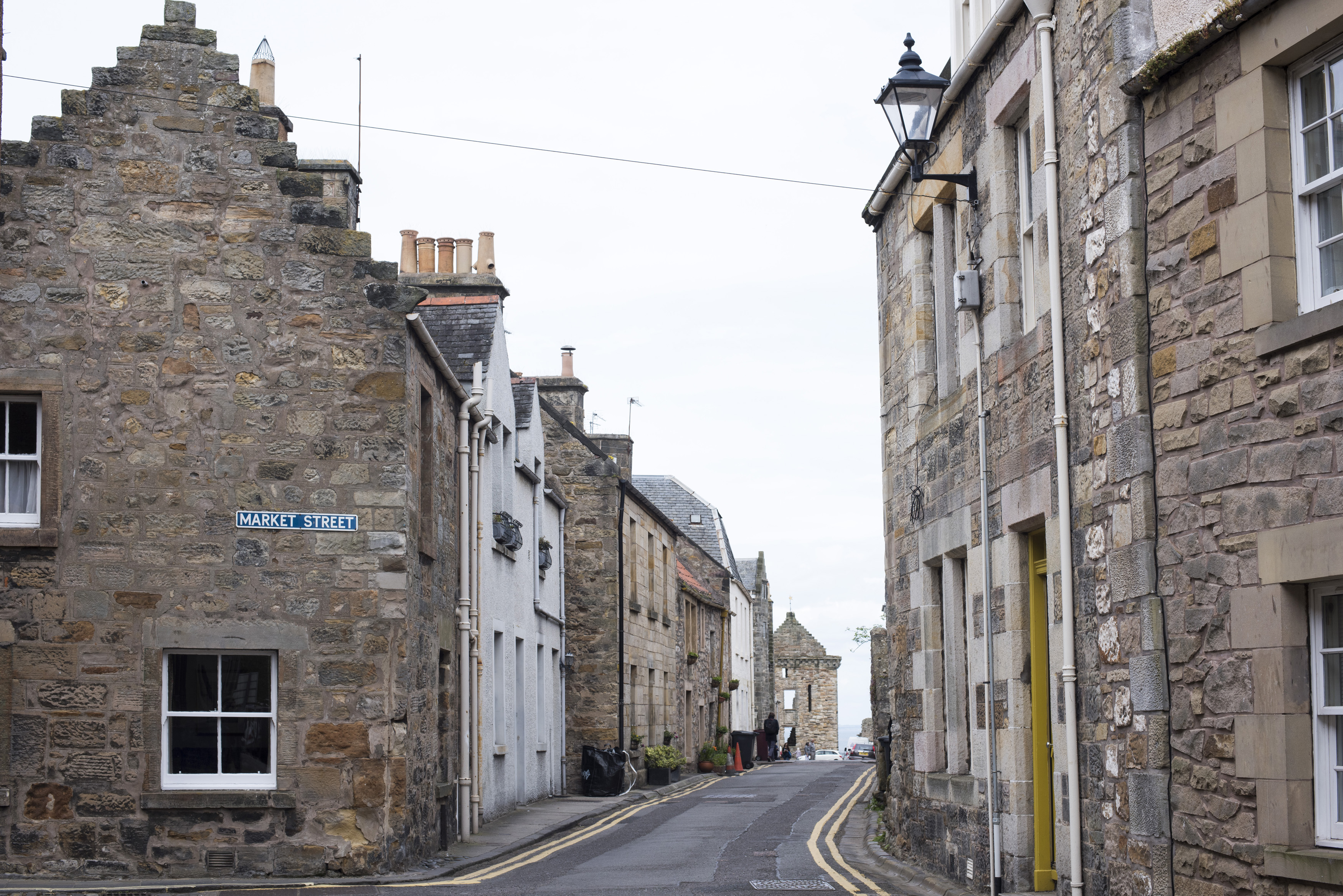 an image of Two rows of old stone brick residential buildings on narrow road in Scotland near Saint Andrews