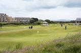 Golfers playing a round of golf on the course at St Andrews, Scotland with the clubhouse visible in the distance under a cloudy grey sky