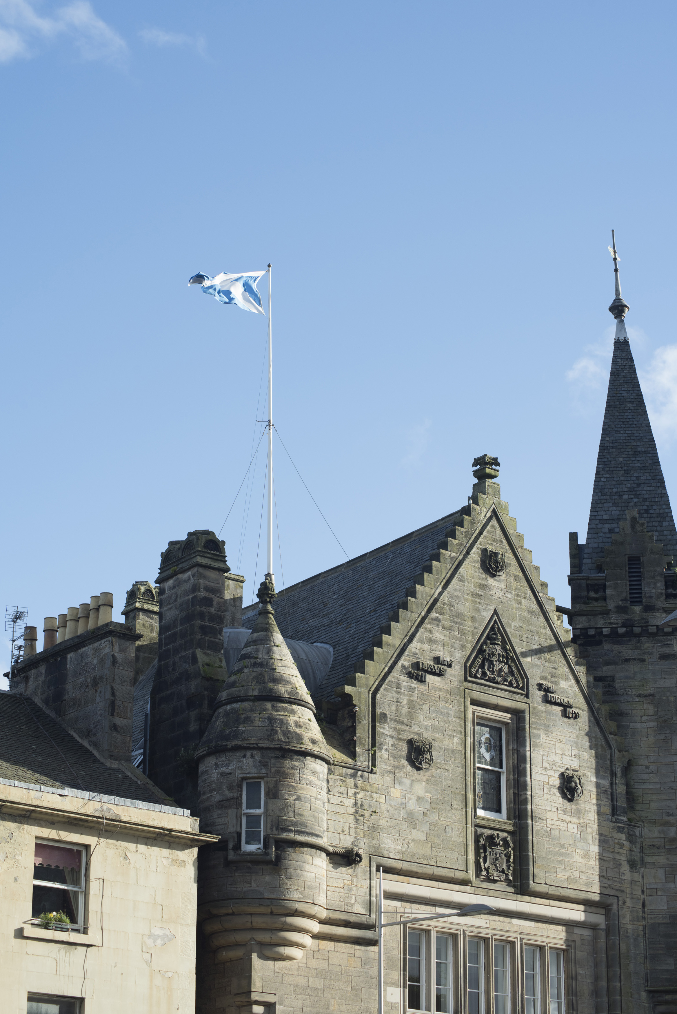 an image of town hall building with with castle like angle tower and flag on top under blue sky in Saint Andrews, Scotland