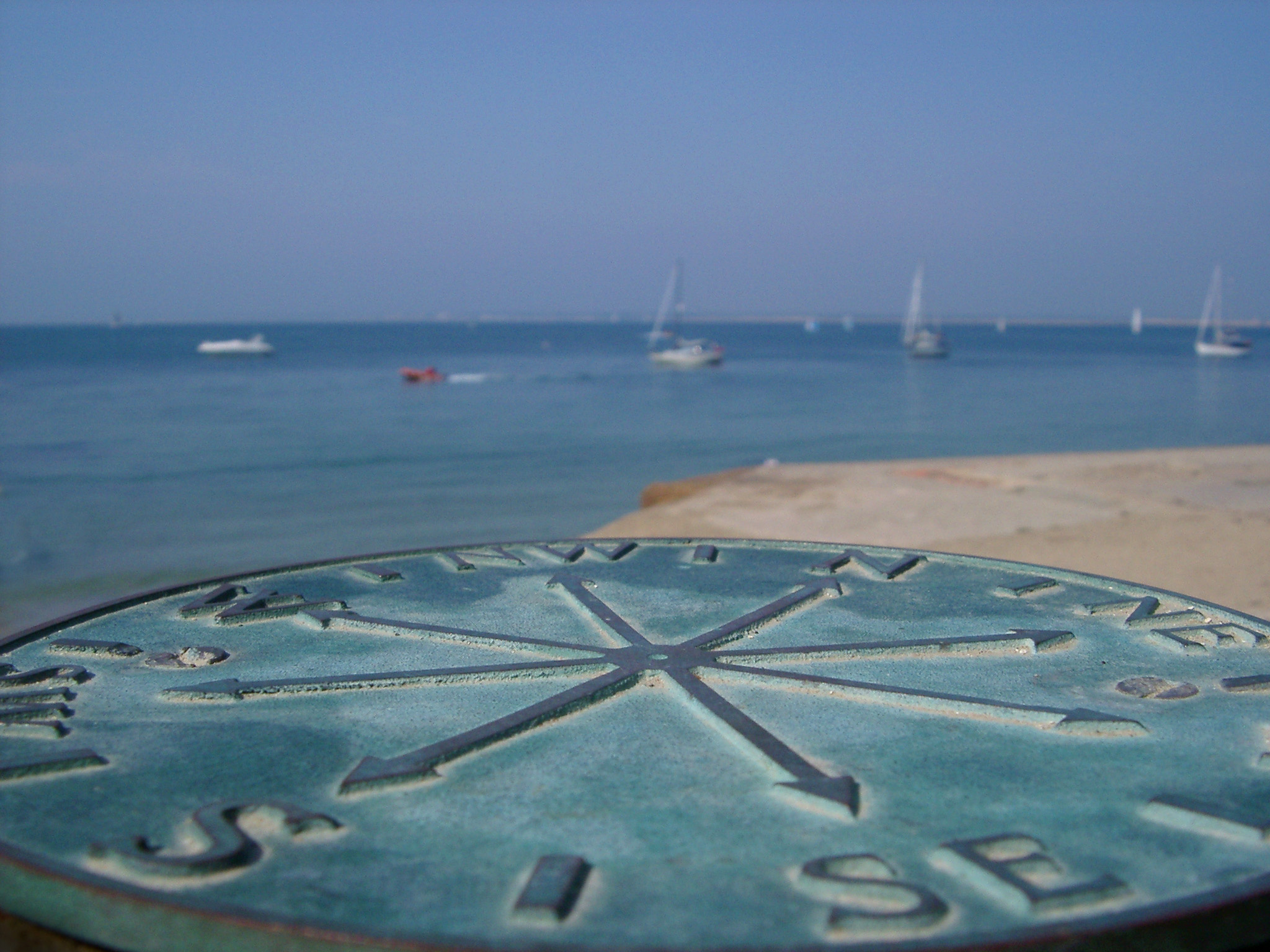 an image of metal plaque marking the points of the compass with yachts on the water in the background