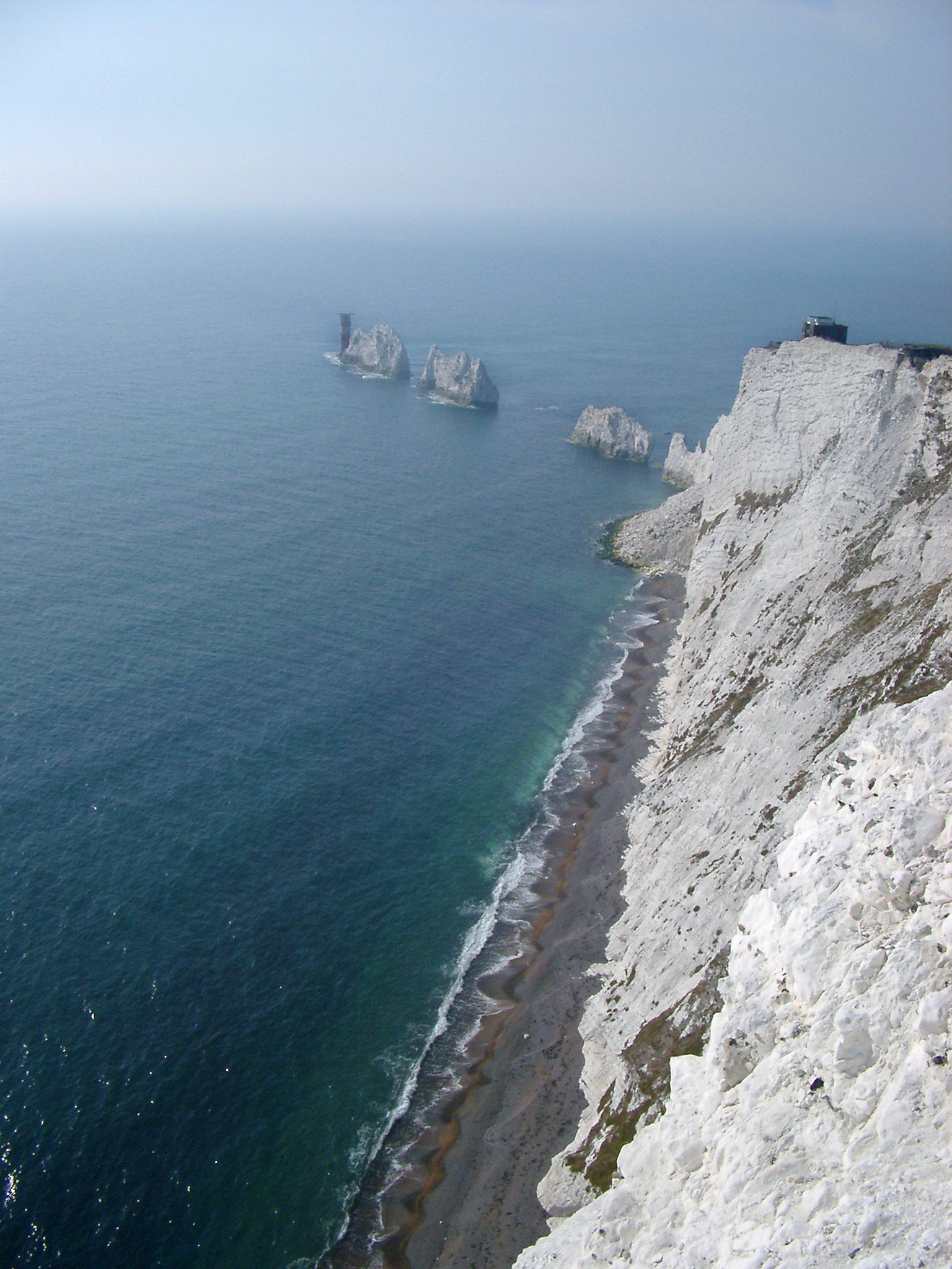 an image of View along the coastline of the Isle of Wight showing the steep cliffs, beach and the Needles, a row of eroded chalk stacks rising from the ocean
