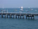Jetty on the Isle of White in a calm ocean with small pleasure craft and sailboats moored offshore on the other side