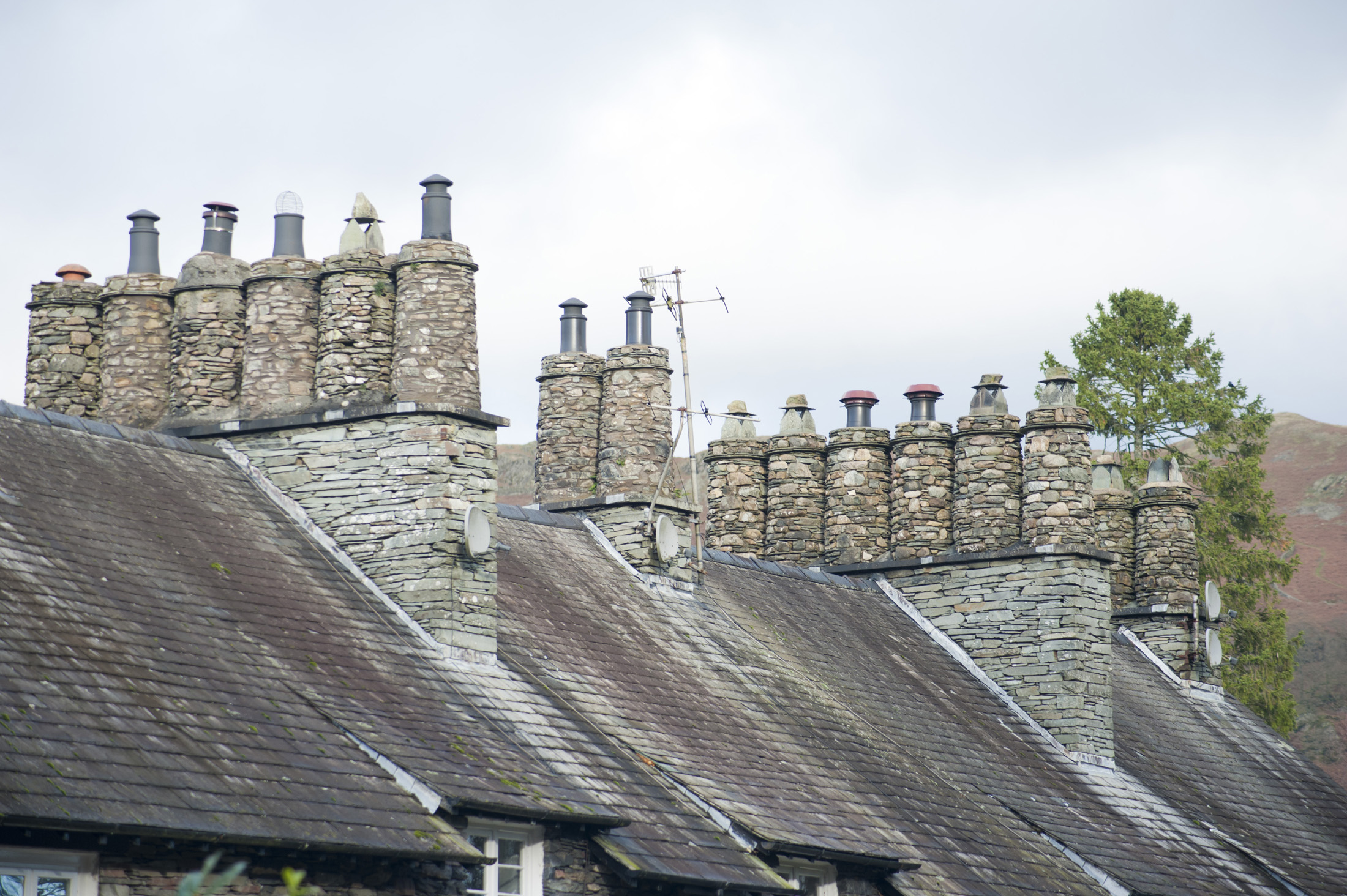 an image of Roofs and traditional cylindrical chimney pots constructed of stone on Cumbrian cottages in the Lake District