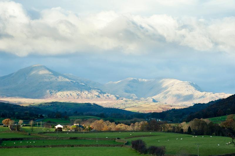 Scenic landscape in the English Lake District with a view of lush green pastiures and farm buildings below a mountain range