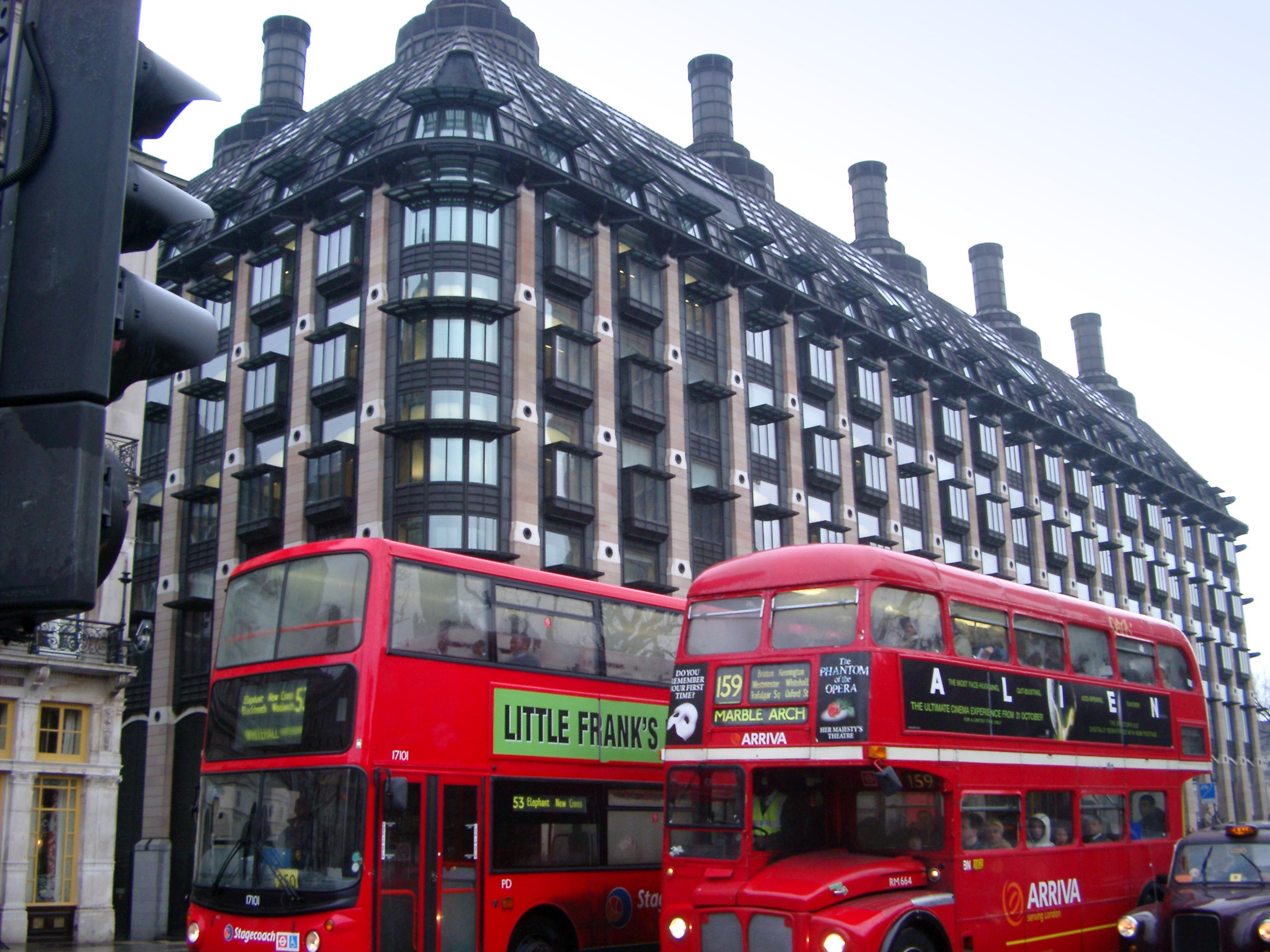 an image of Red London Buses in Tour with Architectural Big European Building on the Street Side.