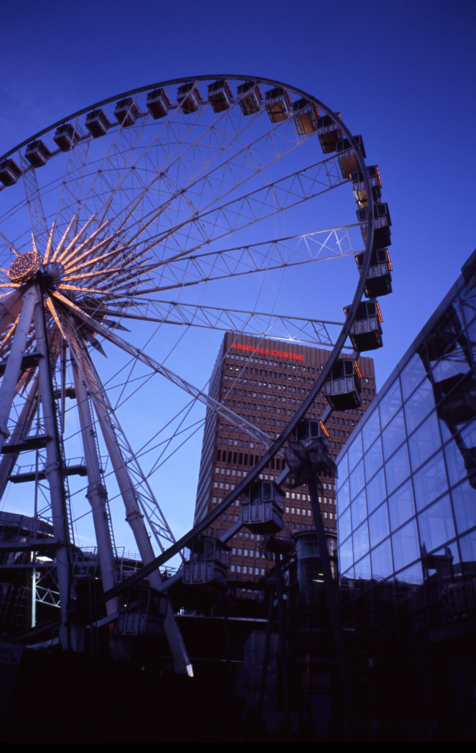 an image of The Manchester Wheel - Famous Transportable Ferris wheel Installation at Piccadilly Gardens, Manchester, England. Captured at Night Time.