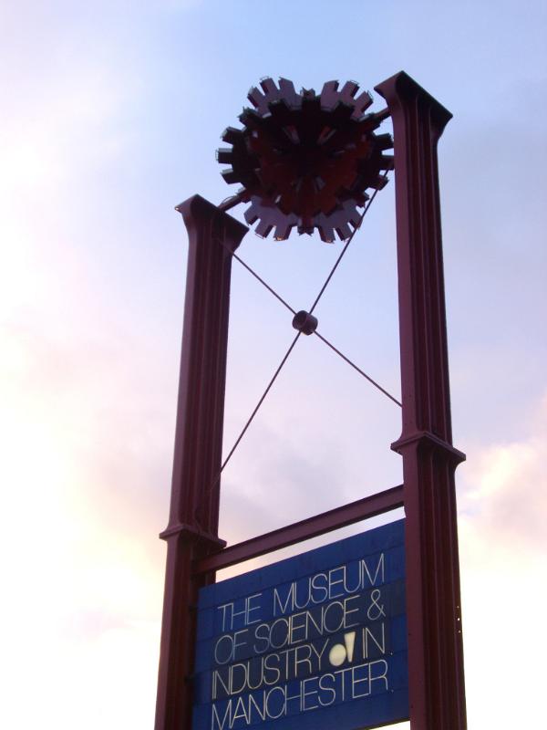 Museum sign board for the Museum of Science and Industry in Manchester silhouetted against a cloudy blue sky