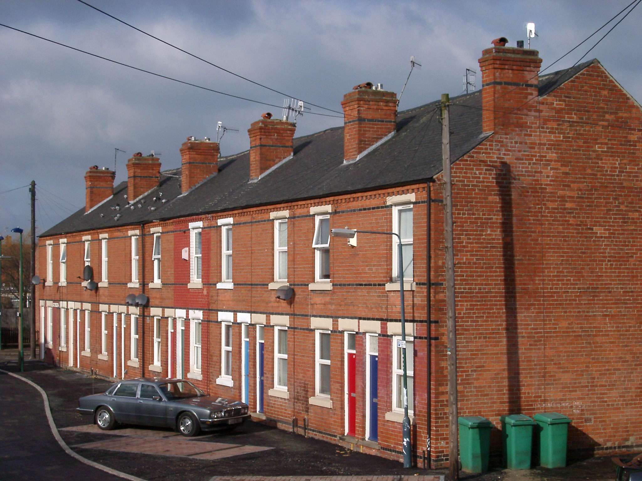 an image of Red brick terraced houses with a Jaguar car parked in front and wheelie bins at the side