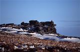 Cold snowy winter walk on Kinder Scout, a moorland plateau and National Nature Reserve in the Dark Peak of the Derbyshire Peak District in England with a rocky outcrop against a clear blue sky