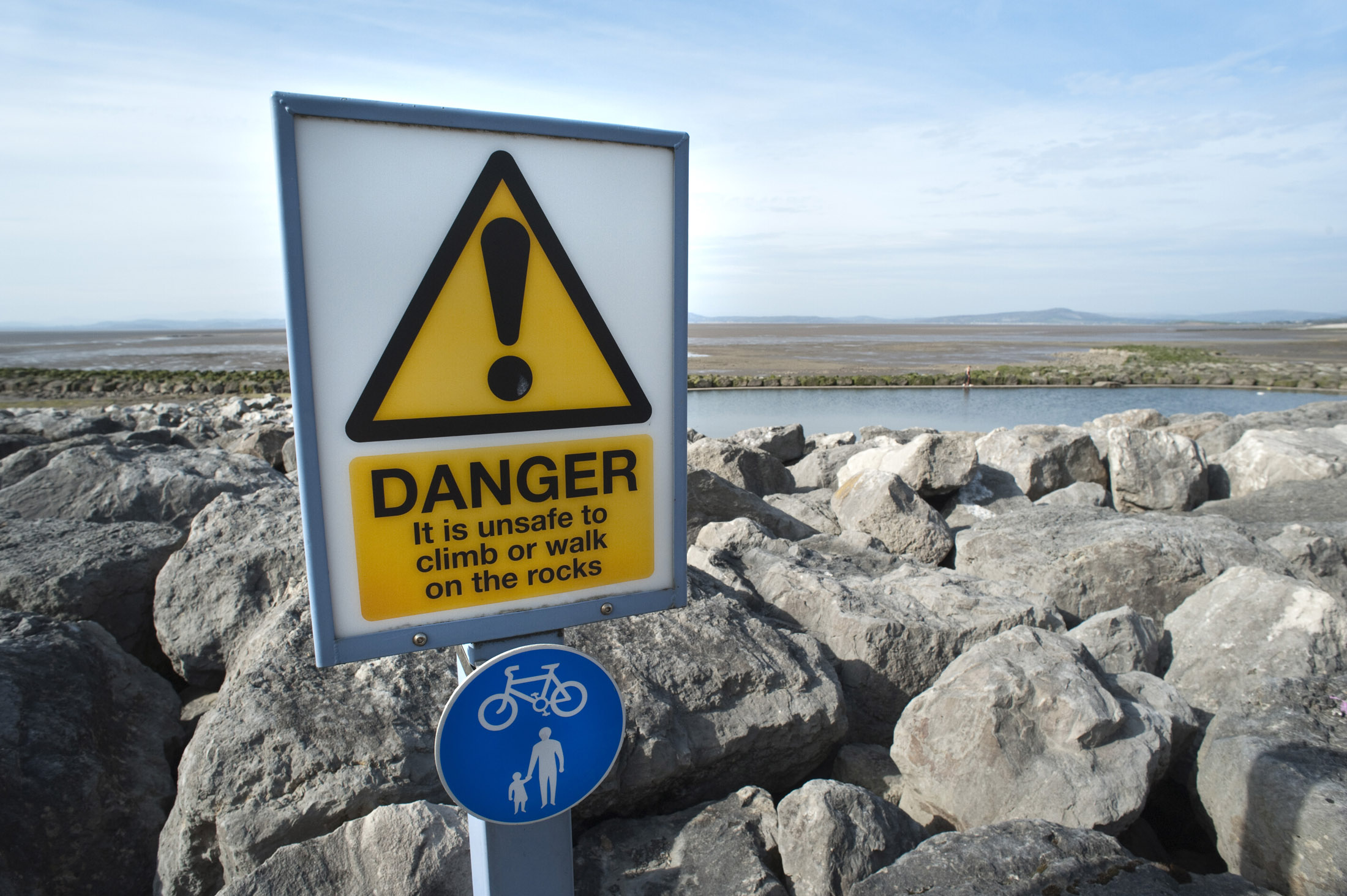 an image of danger sign warning people not to walk on the moraine of boulders scattered along morecambe promenade to defend against the sea
