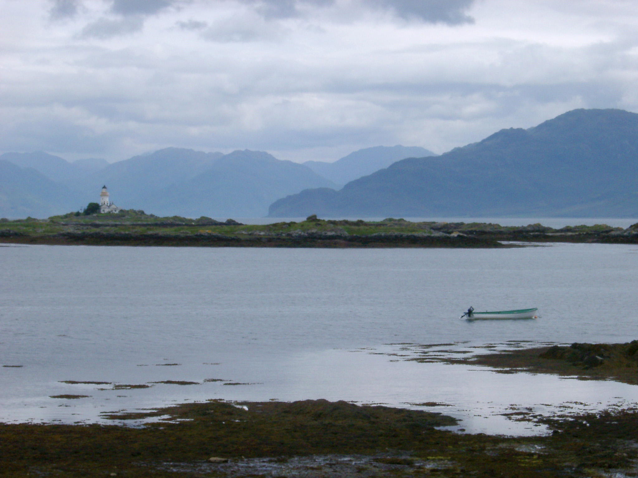 an image of Imposing mountains on the Isle of Skye viewed across water with a lighthouse and small rowboat in the foreground