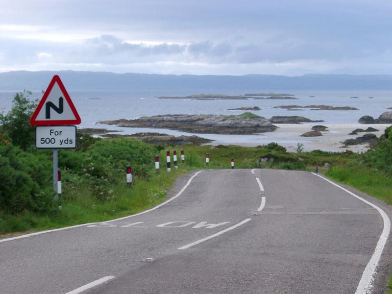 Scottish roads showing a curving bend with a hazard sign warning of bends for 500 yards along a section of the coastline