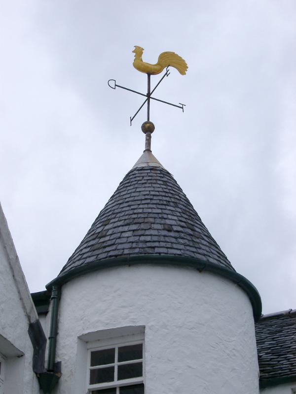 Weather vane in the shape of a cock on top of a small cylindrical tower with a slate roof