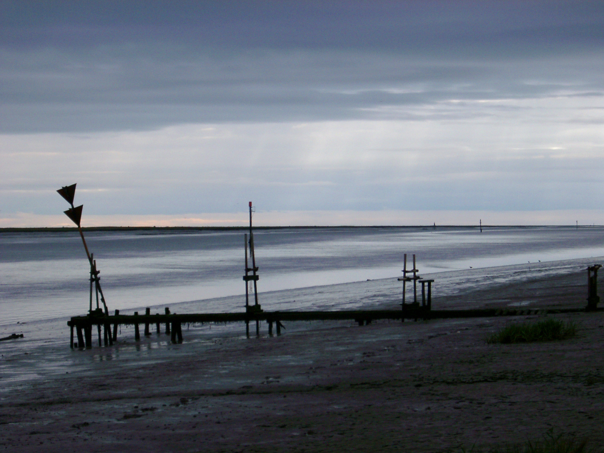 an image of Dark atmospheric landscape of a marine estuary on an overcast stormy day with a silhouette of a small jetty and warning signs on the beach in the foreground