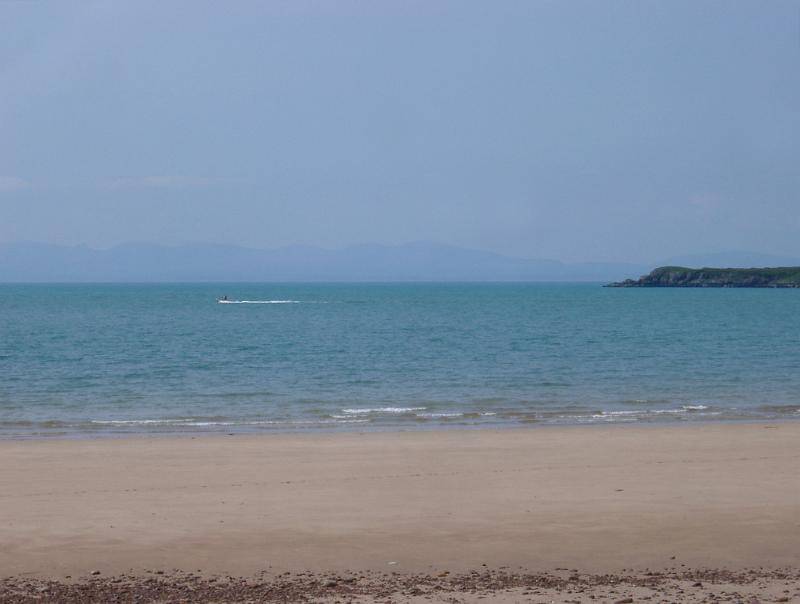 Deserted sandy beach with golden sand and a calm blue sea on the Scottish coast with a headland in the distance