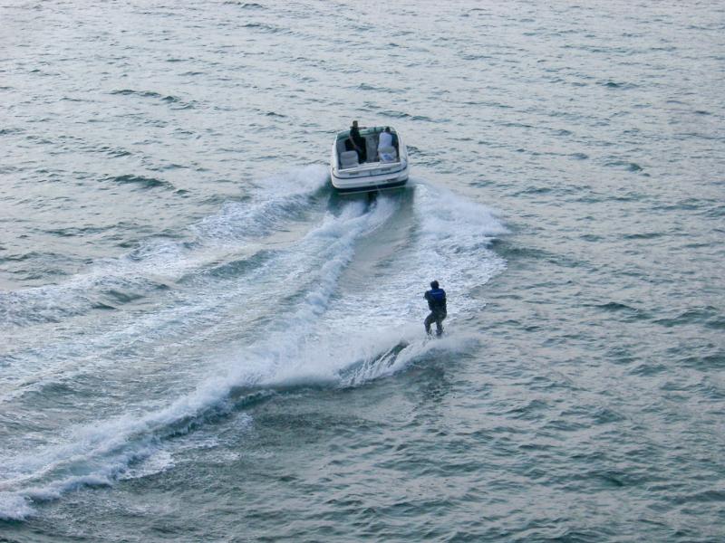 High angle view of a speedboat and skier in a wetsuit speeding away from the camera in a depiction of extreme sport and outdoor activity