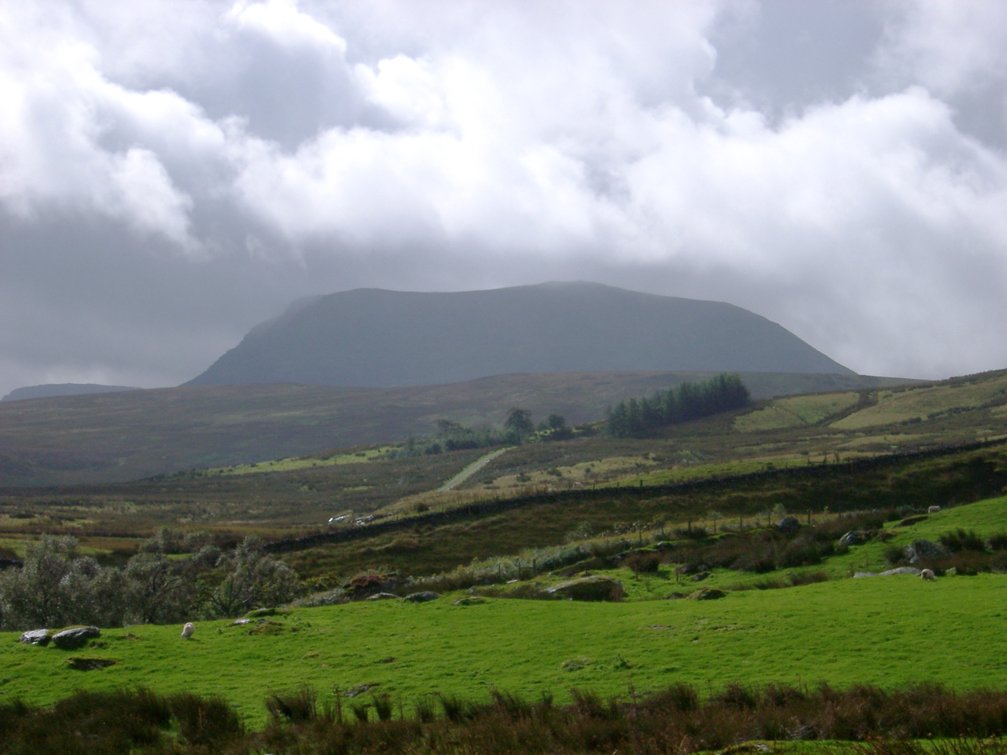 an image of Lush green Wales countryside on a wet day with clouds gathered above a distant hill in a scenic landscape