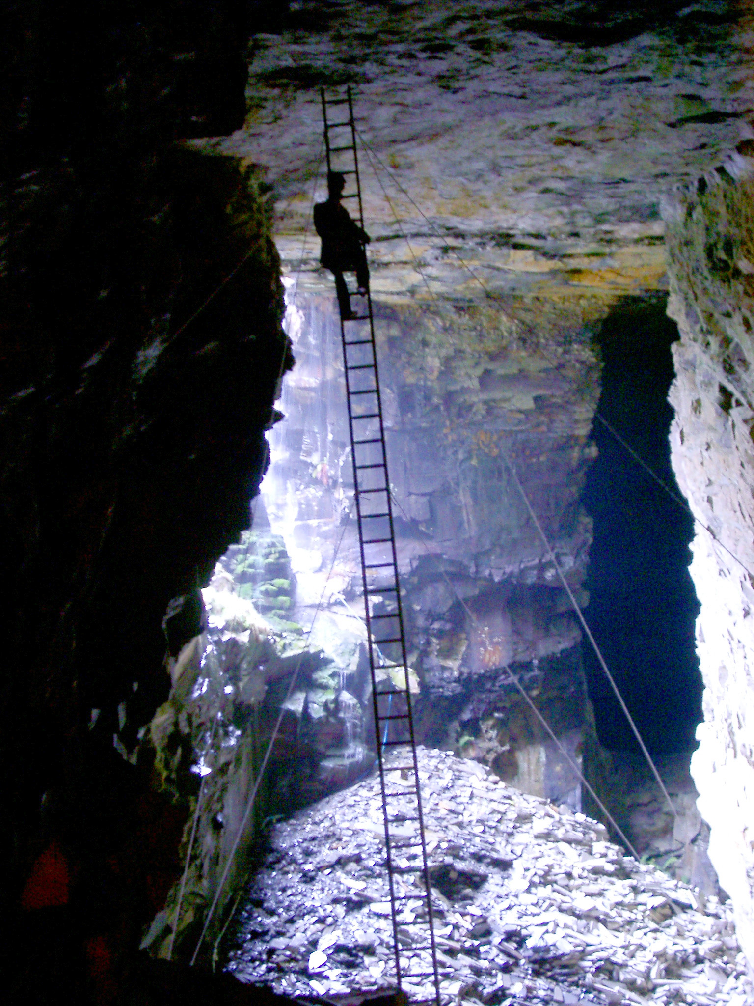 an image of Interior of an old historic slate mine with the silhouette of a man on a ladder suspended from the ceiling and daylight entering from an opening on the side
