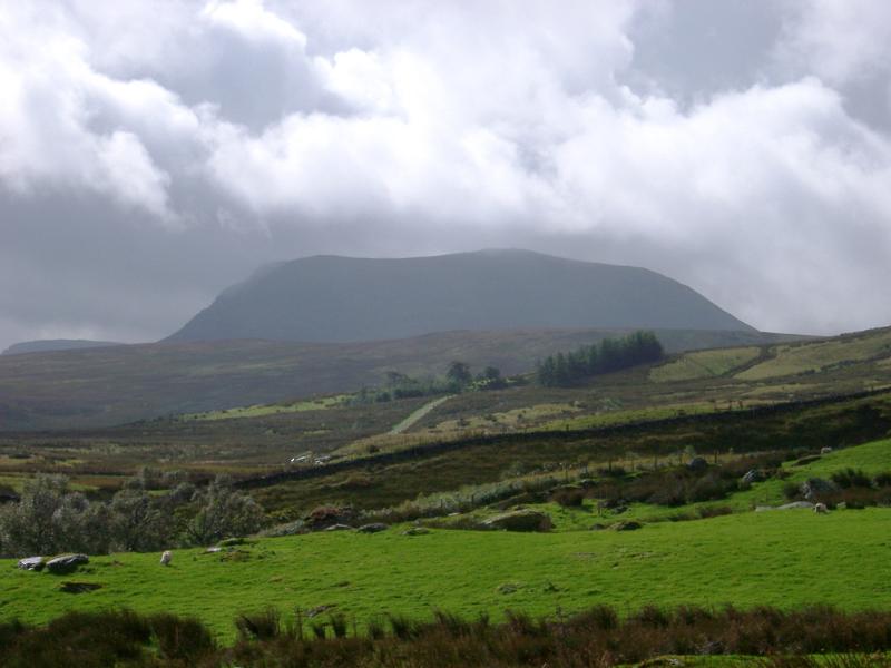 Lush green Wales countryside on a wet day with clouds gathered above a distant hill in a scenic landscape