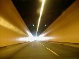 Interior of an underground road tunnel illuminated by overhead lights with a bright flare at the end
