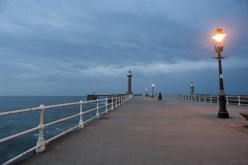 looking along whitbys west pier after sunset lit by the warm glow of streetlights and the last light of the day