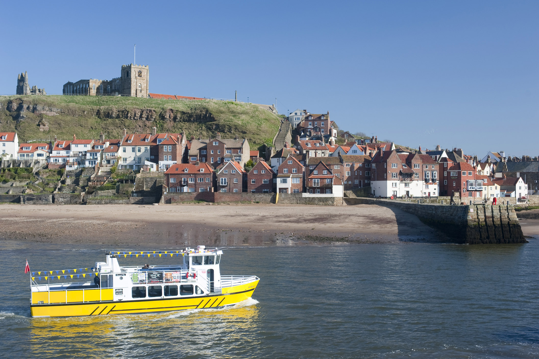 an image of bright yellow trourist cruise boat on whitby lower harbour with the abbey behind