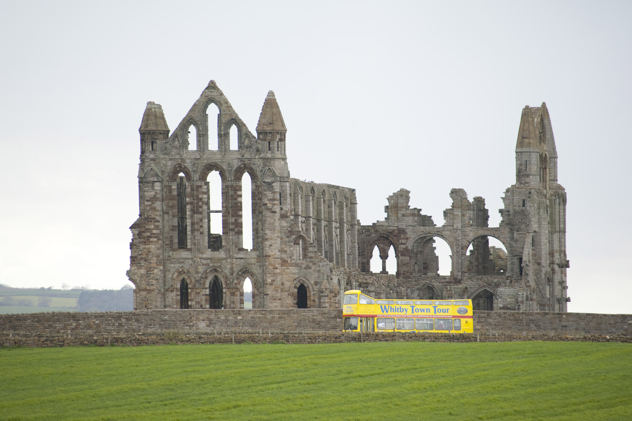 an image of a yellow whitby tour bus drives past the abbey ruins