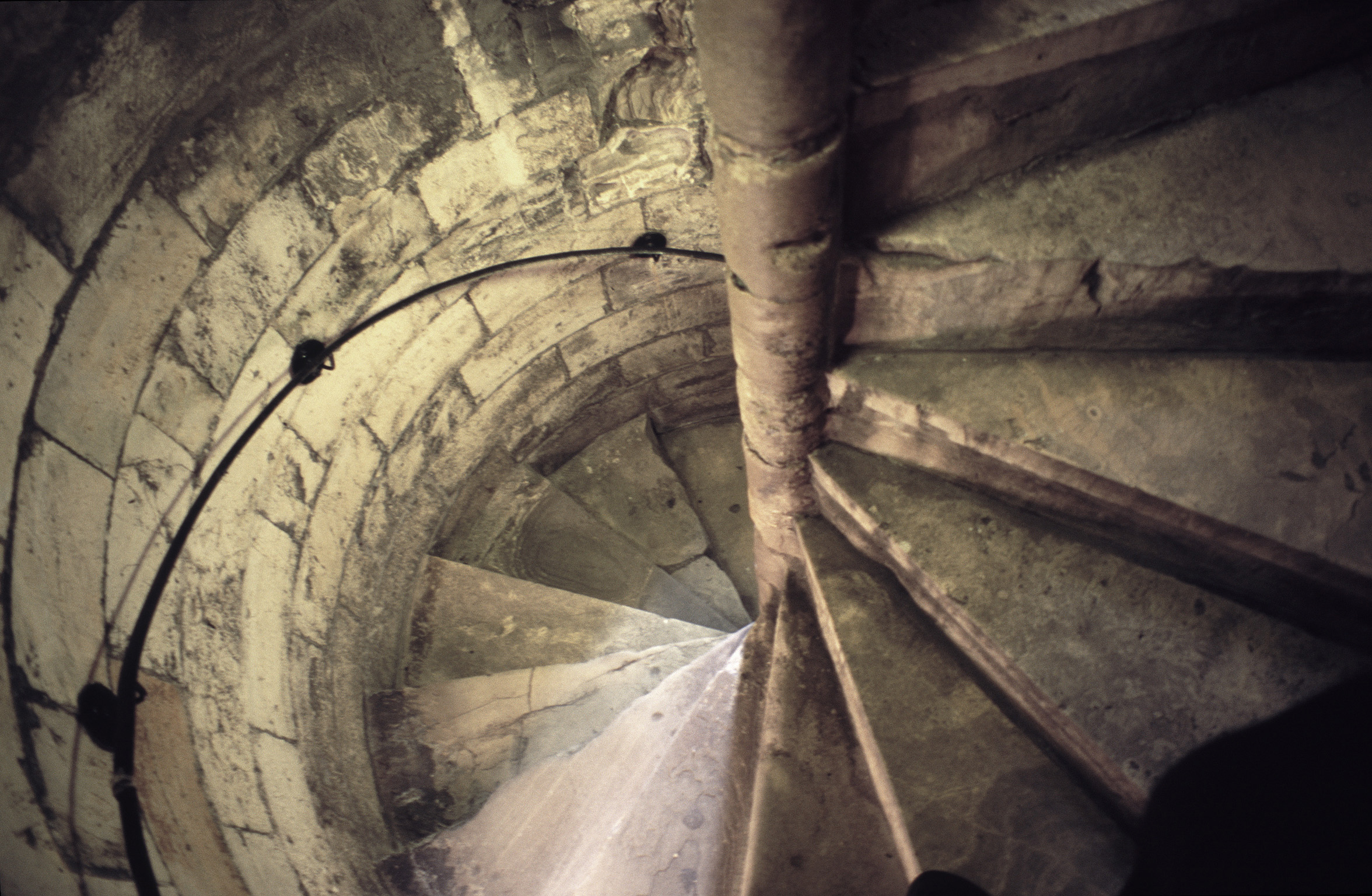 an image of Flight of spiral stone stairs coiling around a central post with a handrail in an ancient circular stone tower, view from inside