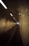 Narrow brick pedestrian underpass lit by overhead fluorescent lights receding into the distance in a straight line