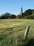 Historic Architectural Australian Church on Grassy Land Surrounded by Green Trees on Light Blue Sky Background.