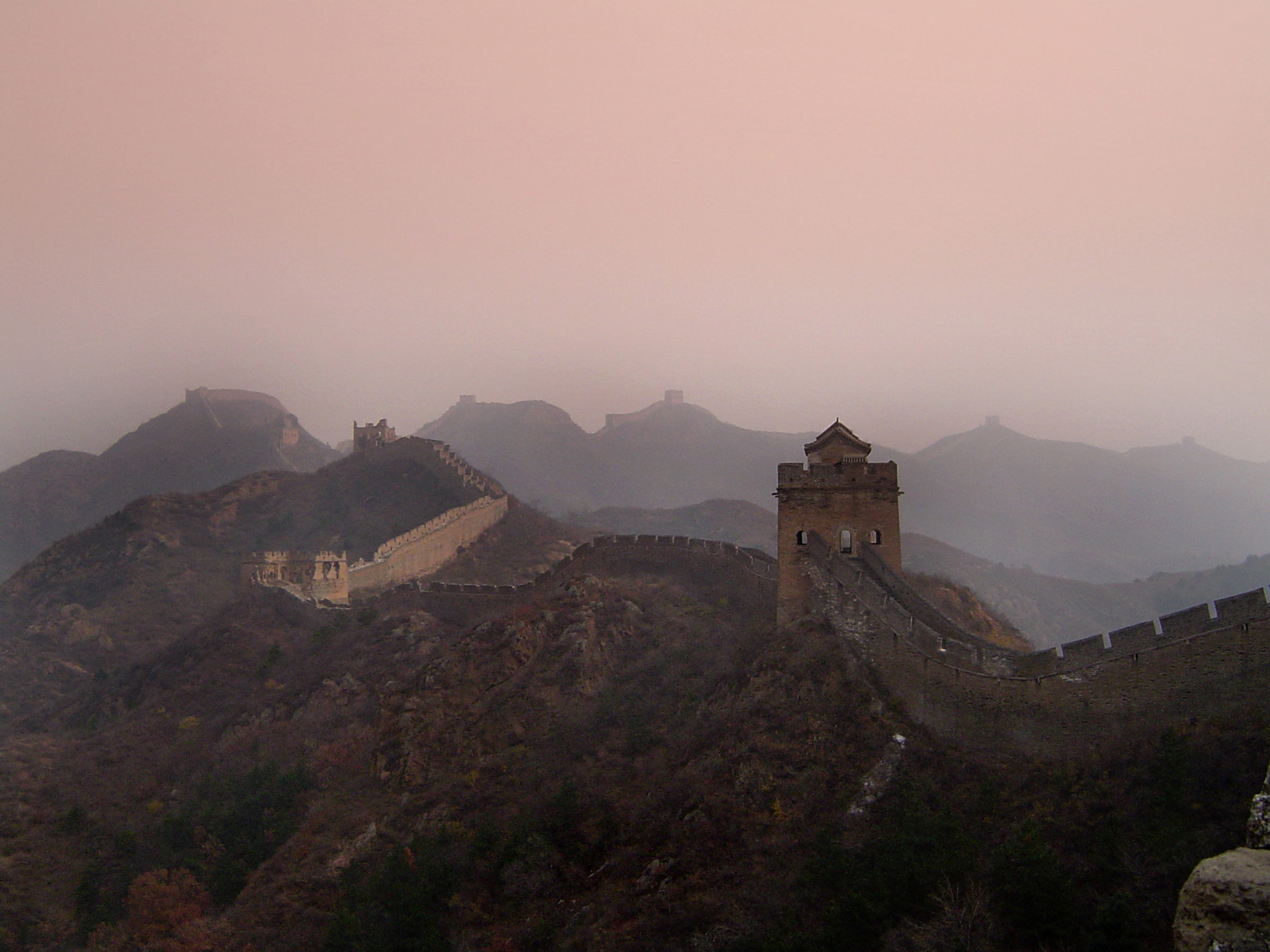 an image of Great Wall of China built to defend the Empire snaking across mountains and valleys on a misty day with smog