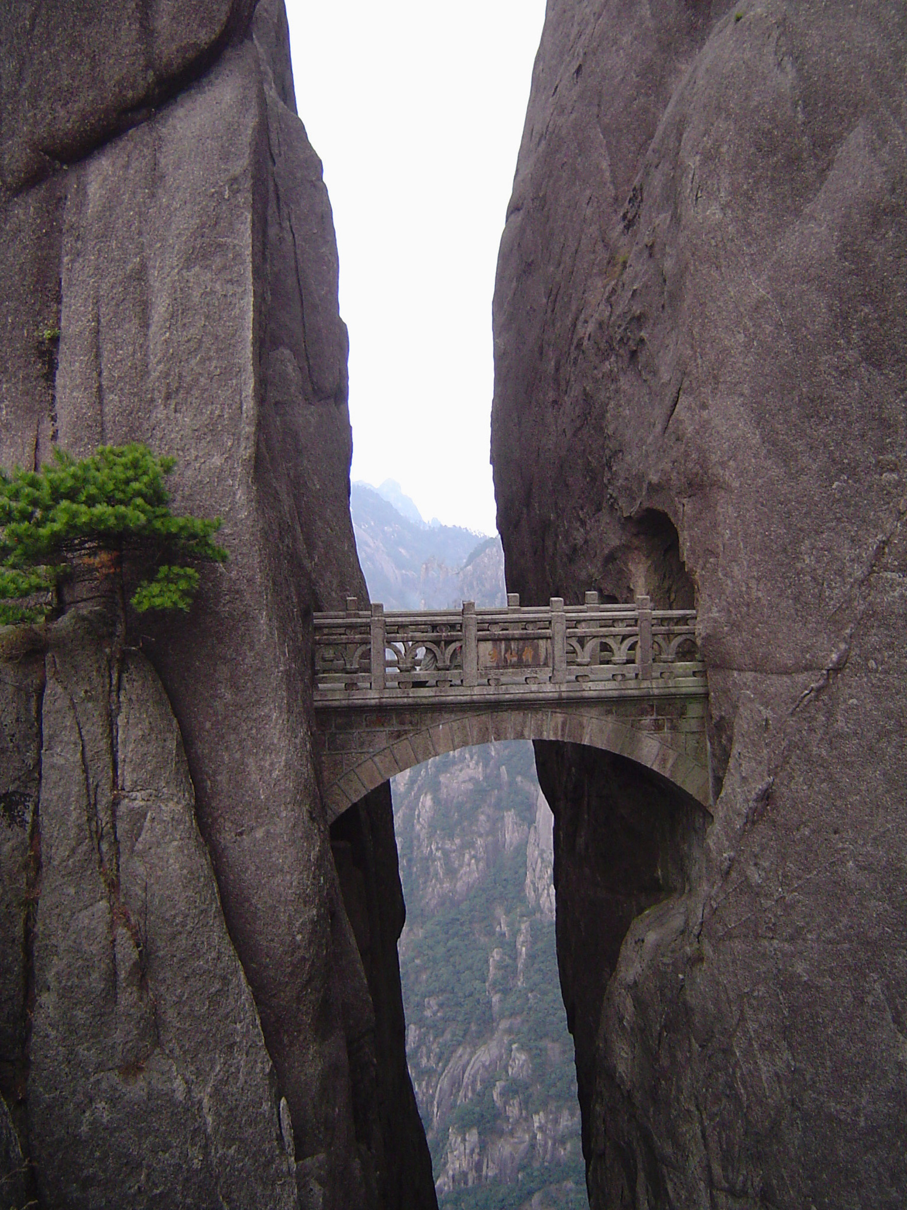 an image of Ornate carved stone bridge, Yellow Mountains, China, spanning a narrow gap between two vertical rock faces