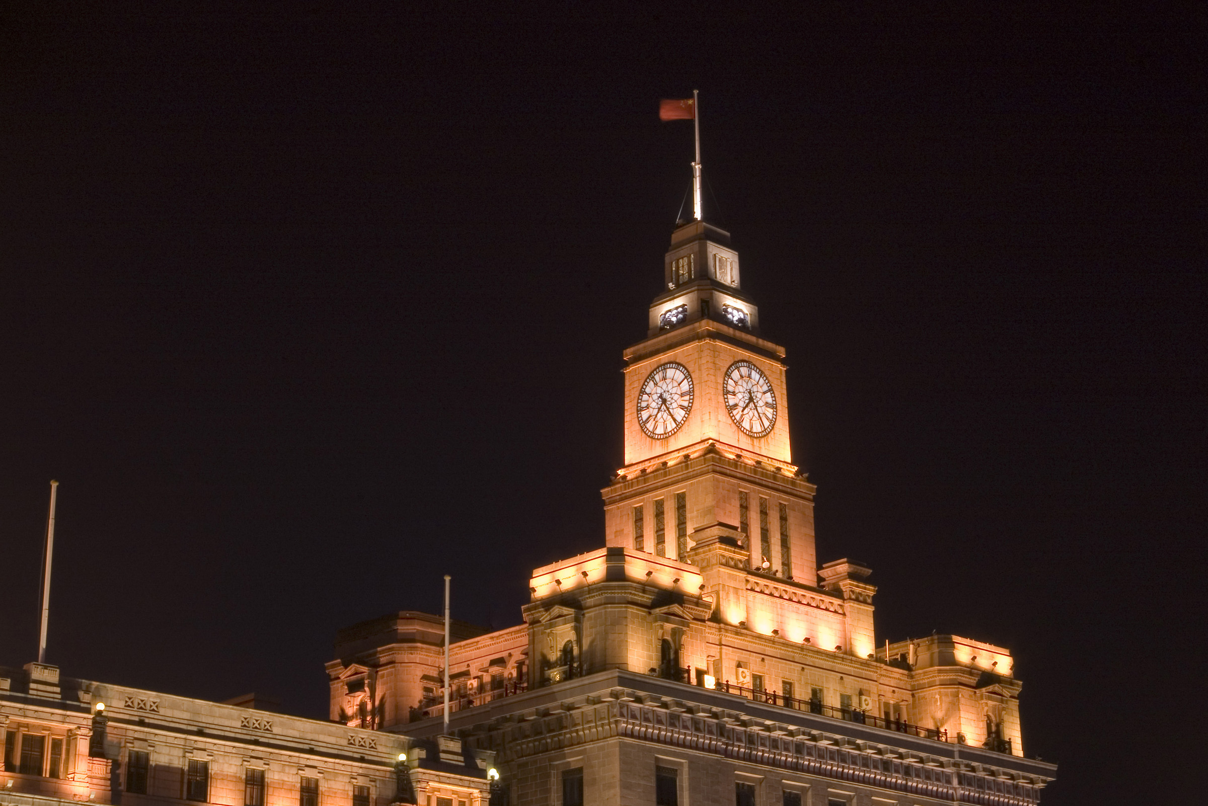 an image of Customs House, or the Bund, Shangai, China illuminated at night with a flag flying at full mast above
