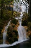Torrent of water cascading down over rocks forming multiple scenic waterfalls in a forest in China
