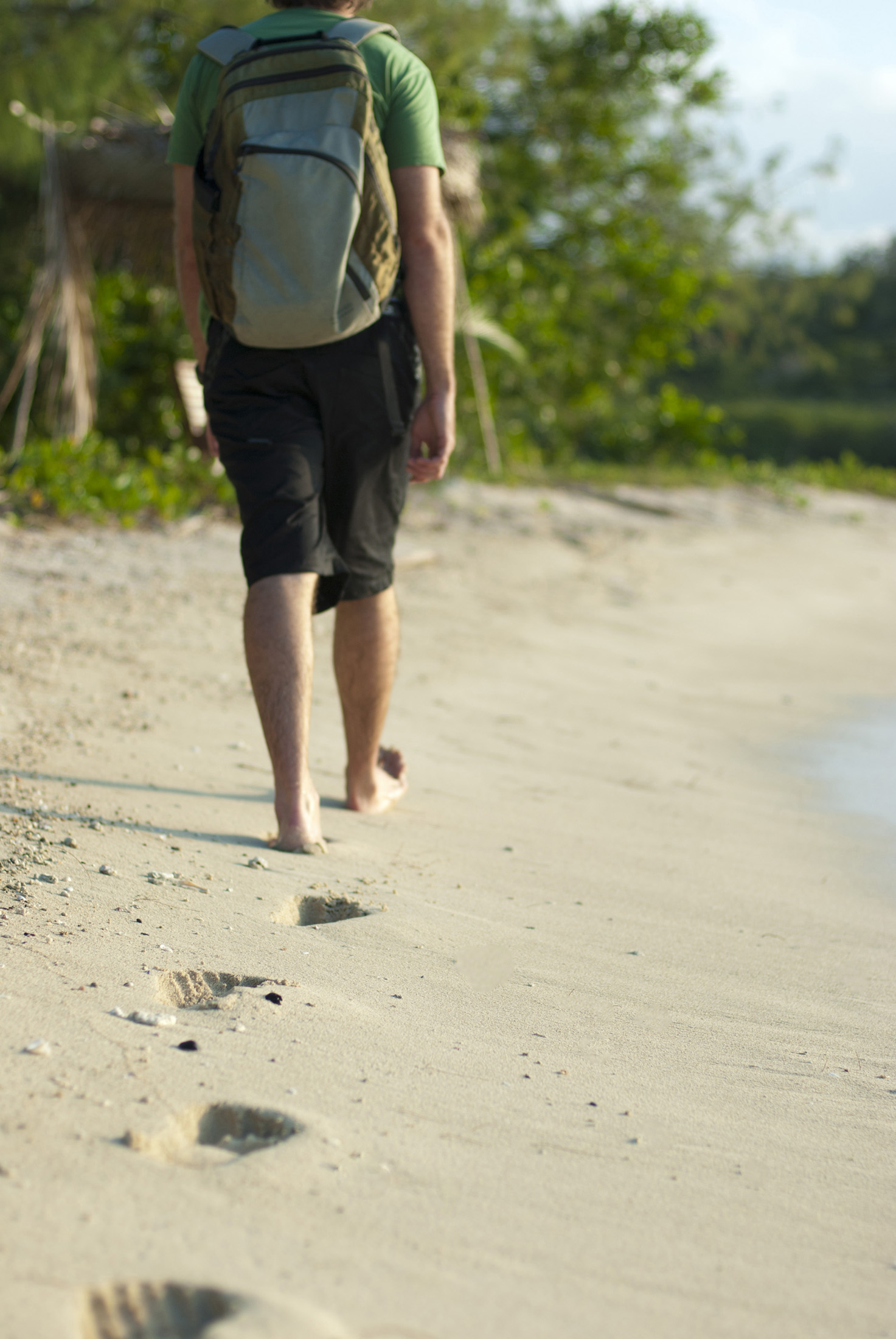 an image of Man wearing a backpack walking away along a sandy beach leaving a trail of footprints
