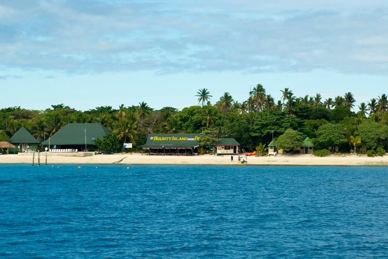 Bounty Island resort, Fiji, on an idyllic tropical island with tourist visible on the sandy beach in front of the buildings