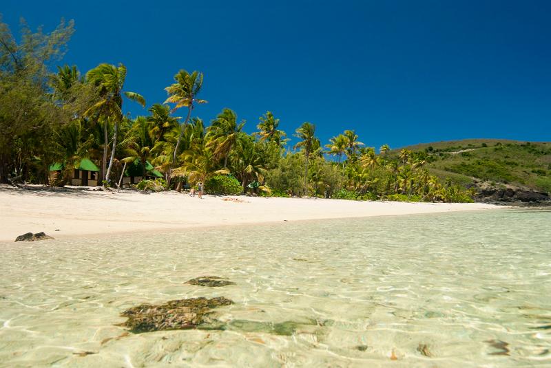 Crystal clear seawater at a tropical beach with golden sands and fringe of palm trees against blue sky